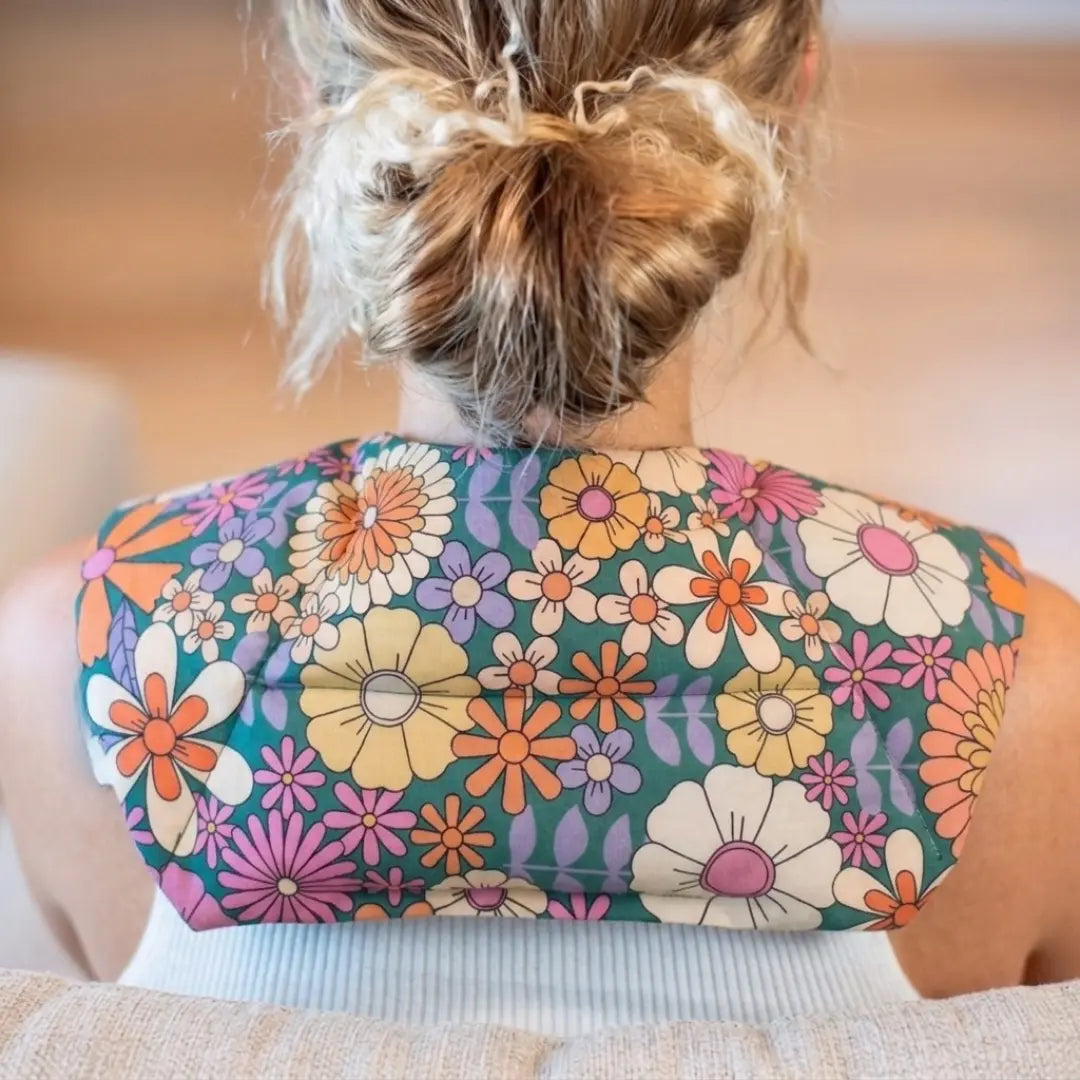 A person viewed from behind wearing a floral-patterned Retro Bloom lupin seed neck heat and cold pack worn around the shoulders