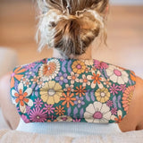 A person viewed from behind wearing a floral-patterned Retro Bloom lupin seed neck heat and cold pack worn around the shoulders